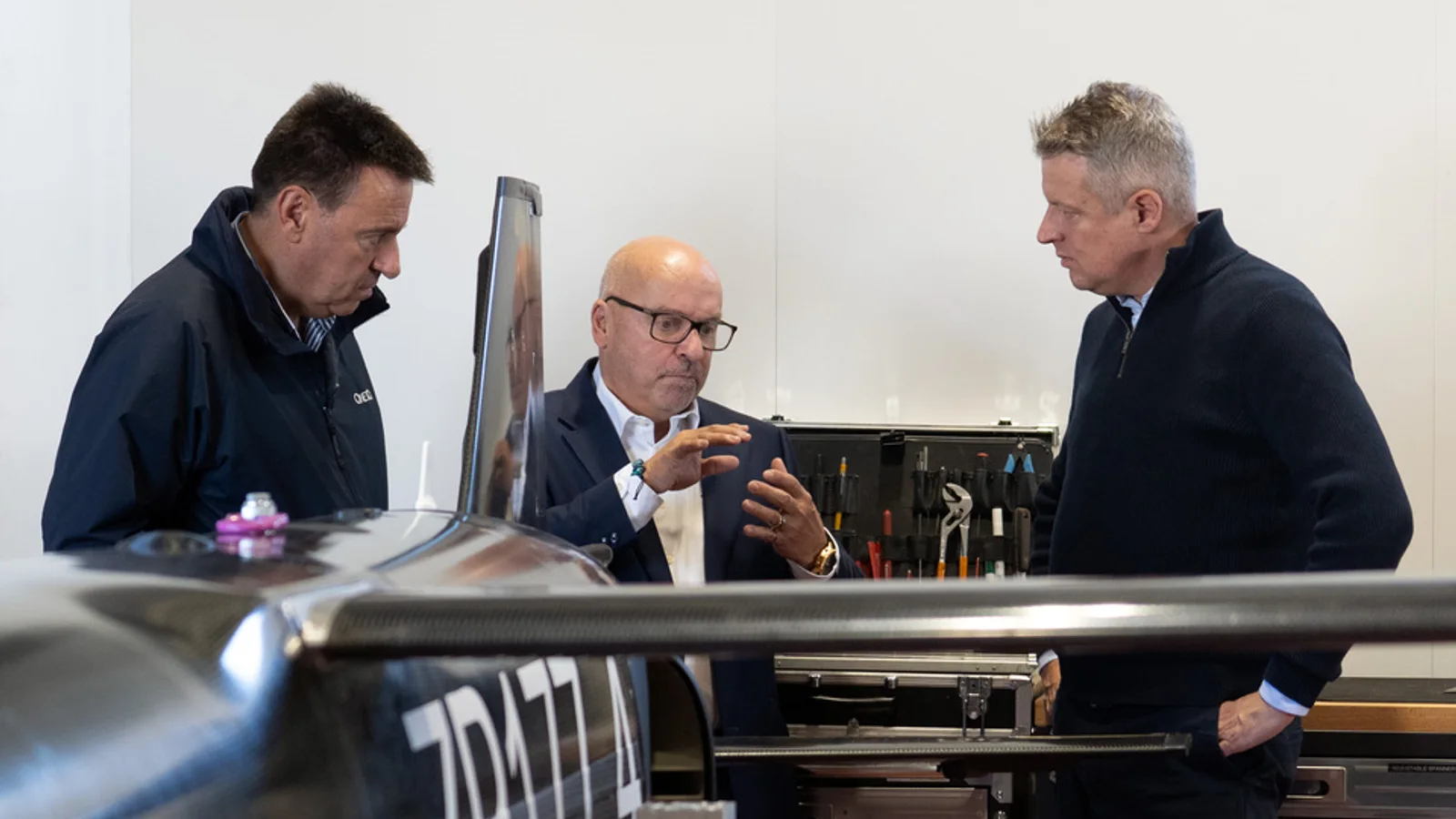 Three men discuss a small aircraft at the UK test-and-evaluation programme visit.