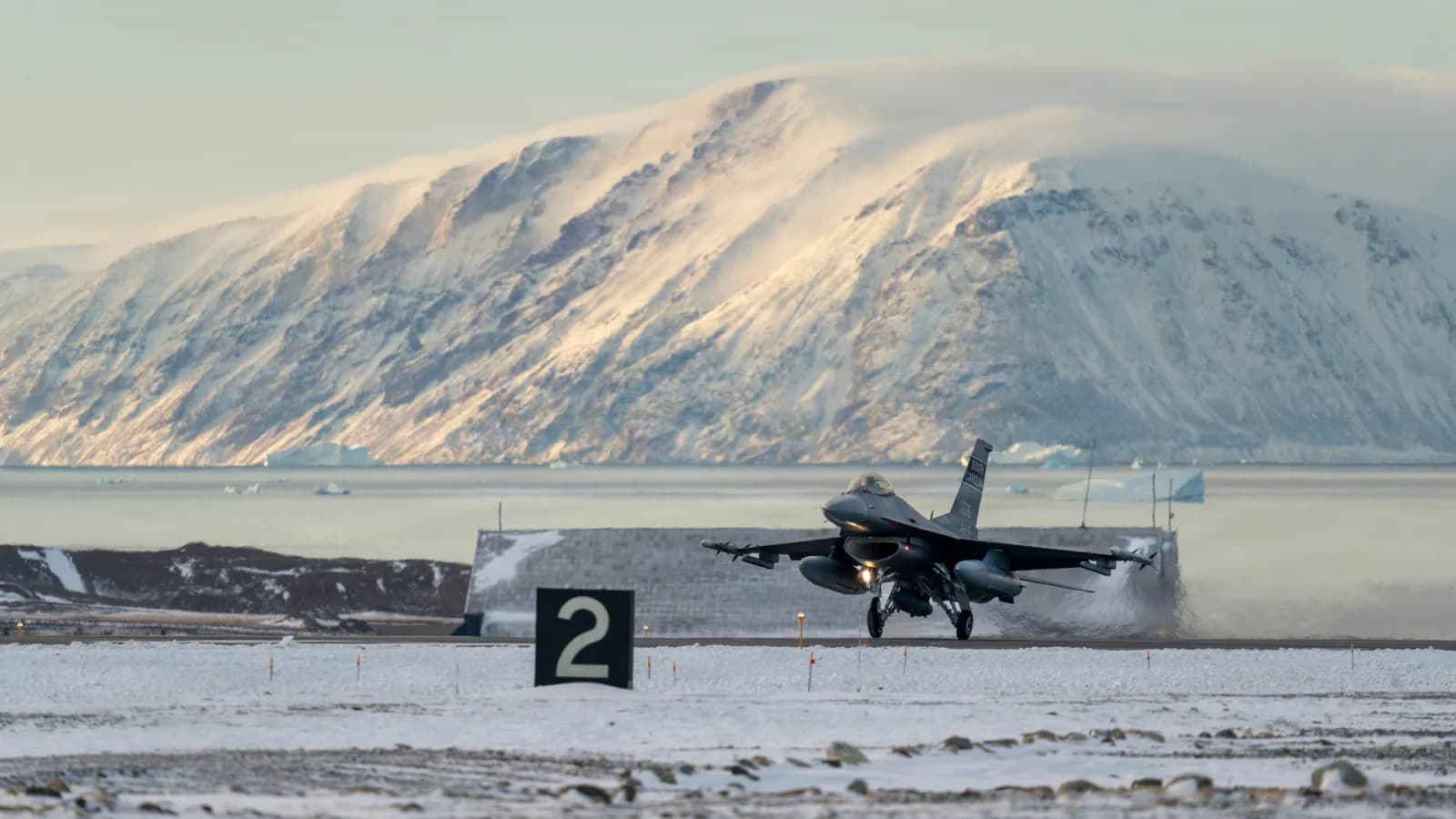 An F-16 lands at Pituffik, Greenland, against snow-covered mountains during NORAD activity in October 2025. Historical contextual photograph.