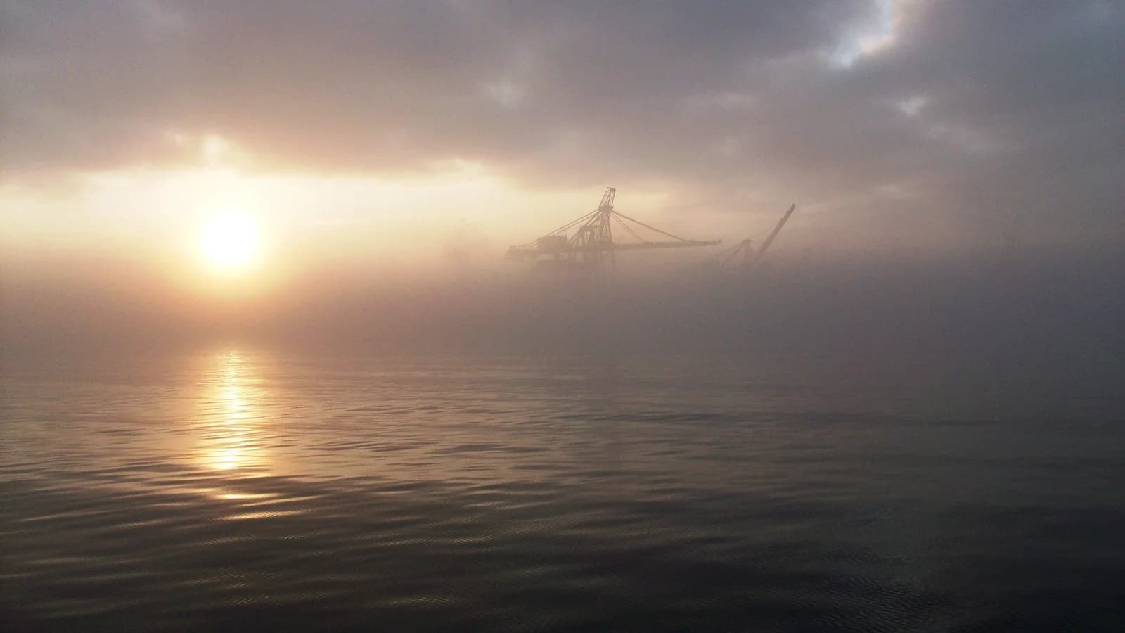 Port cranes emerge through mist above Halifax Harbour at sunset in a historical photograph.