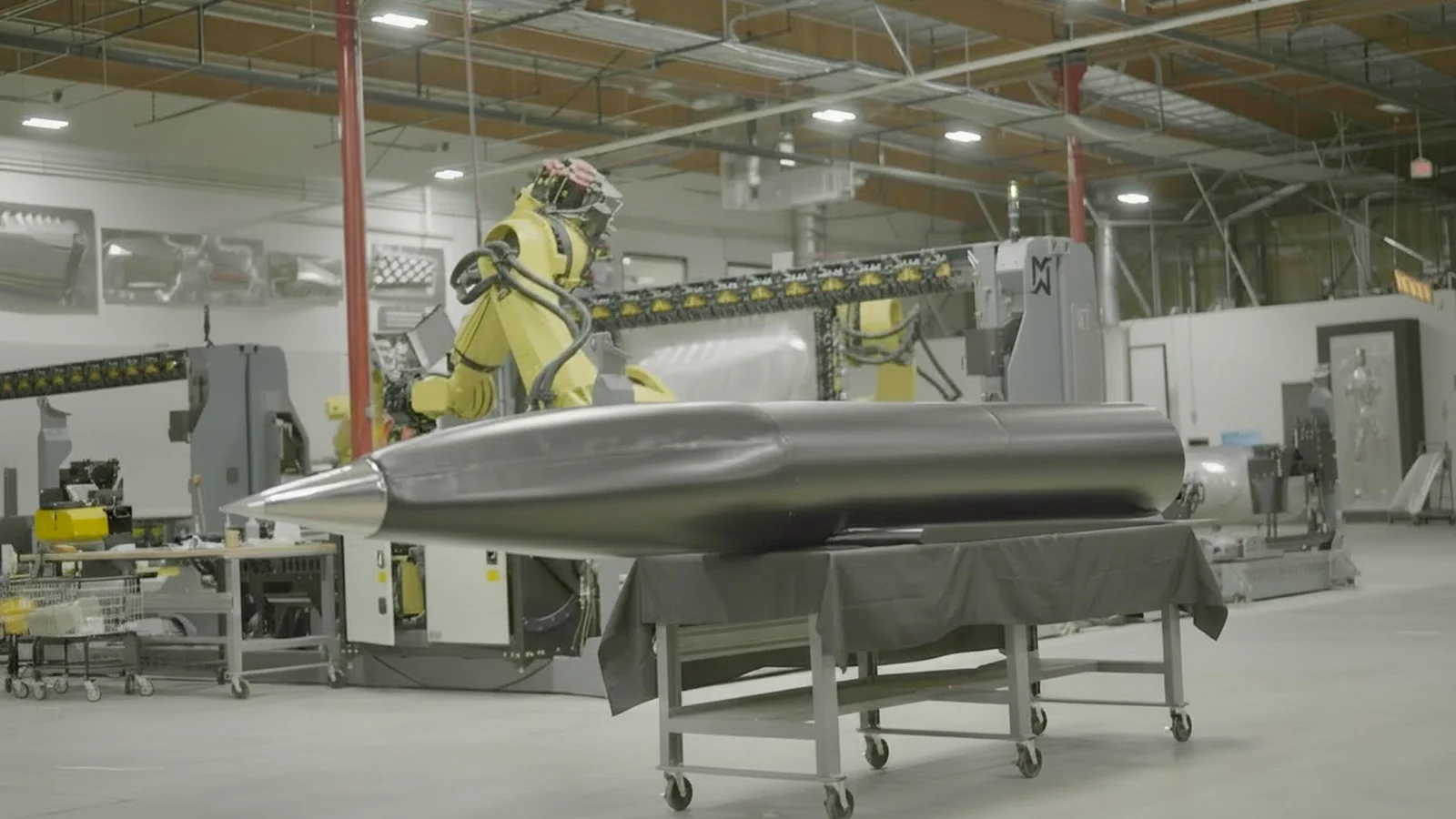 A robotic manufacturing system beside a hypersonic missile fuselage built by Machina
