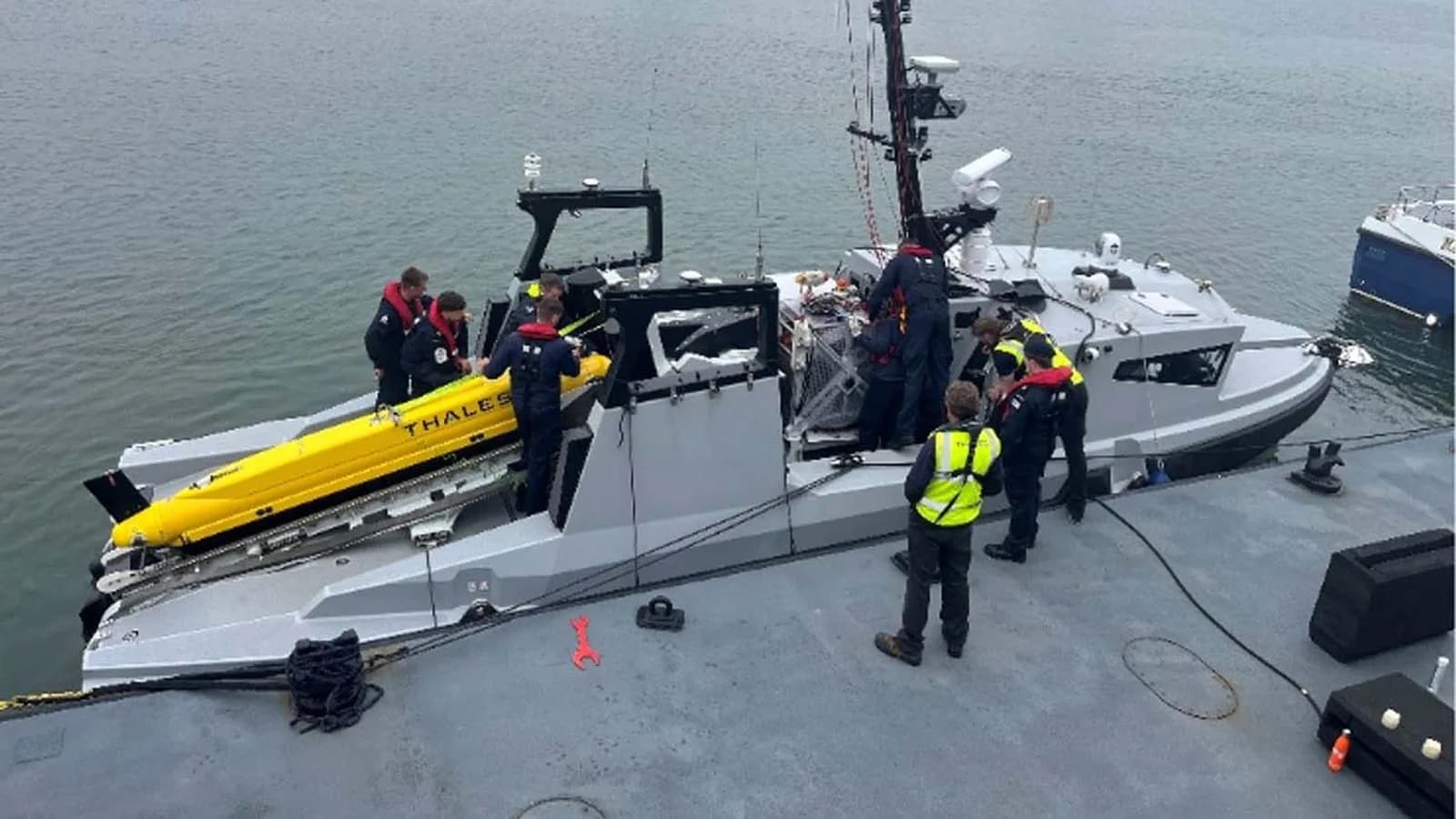 Royal Navy Zulu Unit 1 staff work with a yellow Thales minehunting system aboard an uncrewed vessel.
