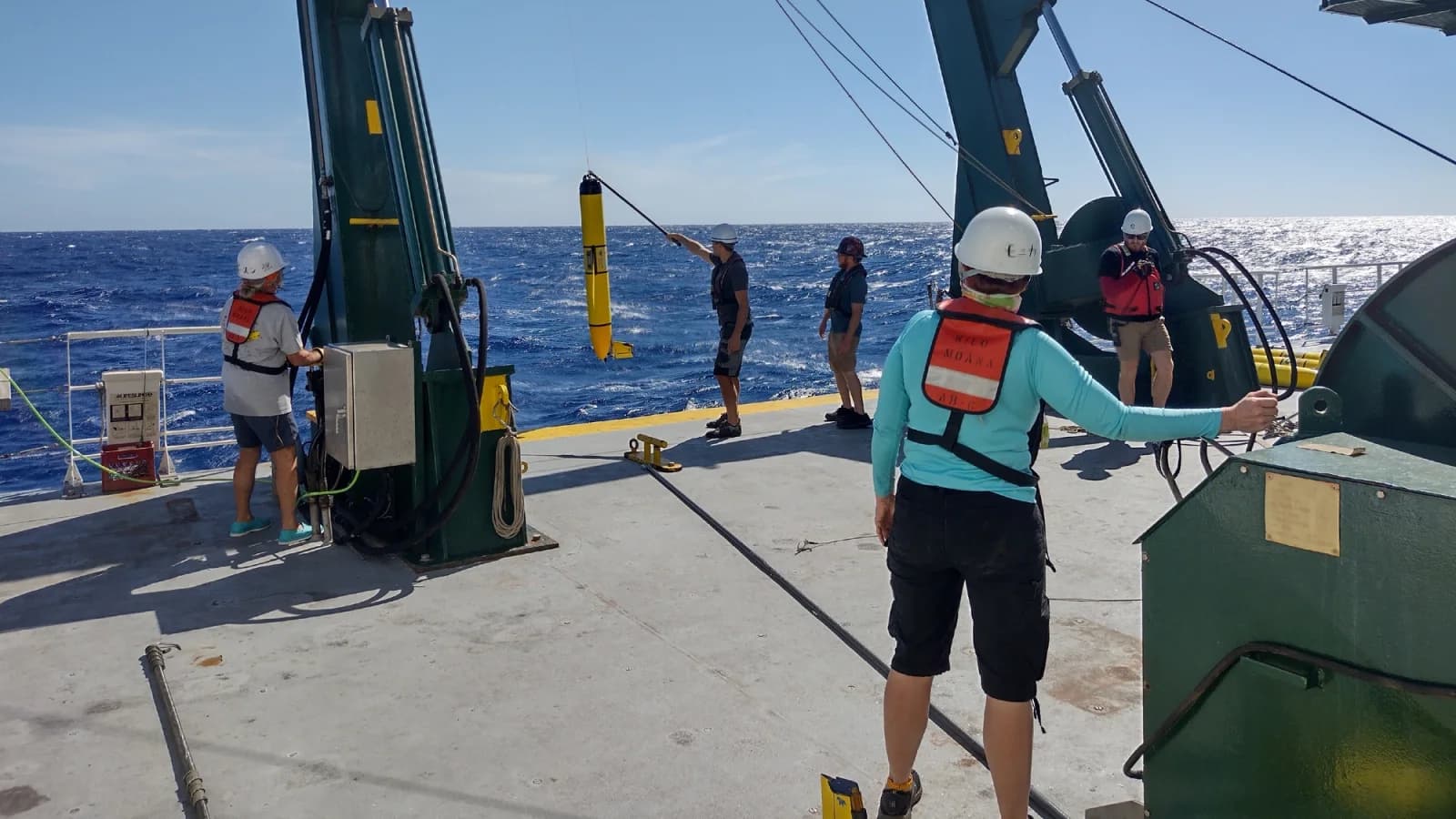 Crew handle a suspended glider aboard RV Kilo Moana during a Pacific recovery effort in October 2021